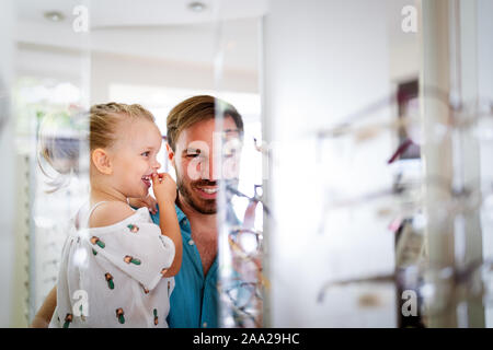 Health care, eyesight and vision concept. Little girl choosing glasses with father at optics store Stock Photo