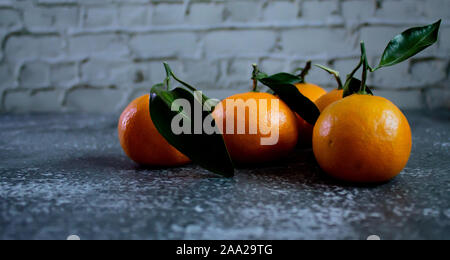 Gray concrete background with a brick wall, tangerines with leaves and twigs view from the top. New Year, in the style of health. Stock Photo