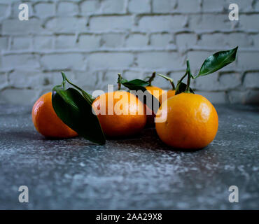 Gray concrete background with a brick wall, tangerines with leaves and twigs view from the top. New Year, in the style of health. Stock Photo