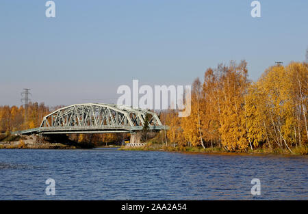 A steely railway bridge over a lake on a sunny autumnal day. Trees have got their yellow color Stock Photo