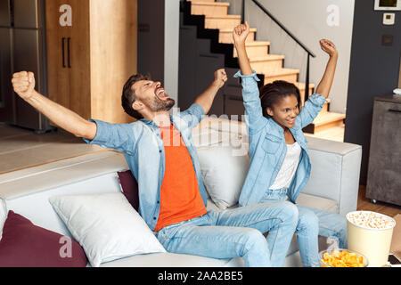 Young adult woman and man raised hands up, sitting at home Stock Photo