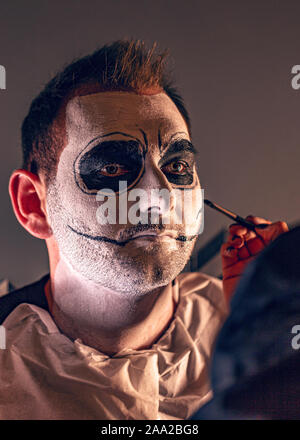 Make up artist applying products painting a young man before Halloween party Stock Photo
