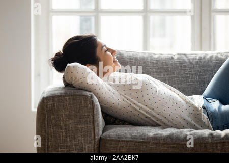 Happy millennial tranquil indian woman lying on comfortable couch. Stock Photo