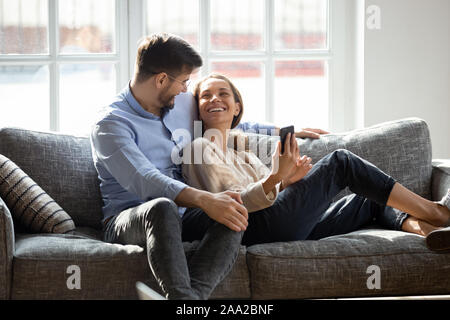 Laughing millennial mixed race woman showing funny video to husband. Stock Photo
