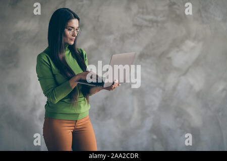 Photo of serious confident smart clever woman browsing through laptop in orange pants typing to find necessary information isolated grey wall color Stock Photo