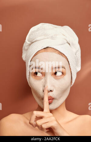 Beautiful woman with clay facial mask over orange background. Beauty treatment and spa concept. Stock Photo