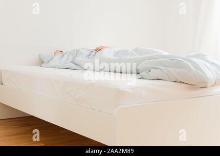 Part of the home or hotel interior, man sleeping on a white bed with blue linens in the morning Stock Photo