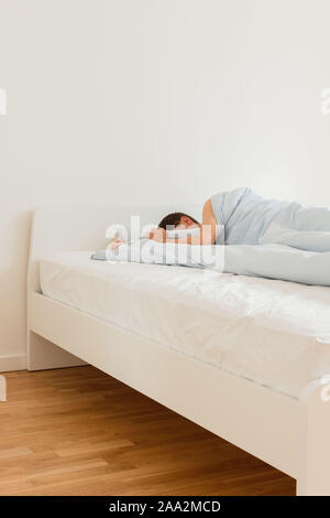 Part of the home or hotel interior, man sleeping on a white bed with blue linens in the morning Stock Photo