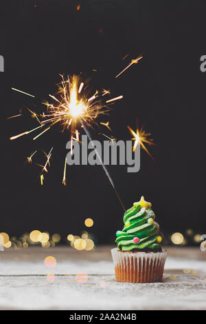 Vanilla cupcake with christmas bokeh and sparkler on dark background; holiday background with copy space Stock Photo