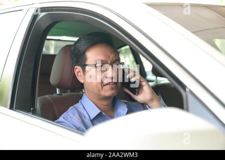 Asian chinese businessman smiling and talking on his cell phone inside his car Stock Photo