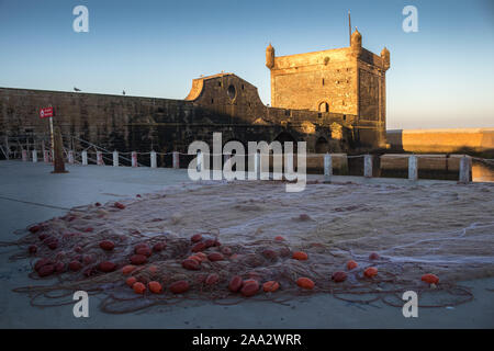 Early morning with enligted tower of the fortification. Outspread fishing net in the foreground. Blue sky. Essaouira, Morocco. Stock Photo