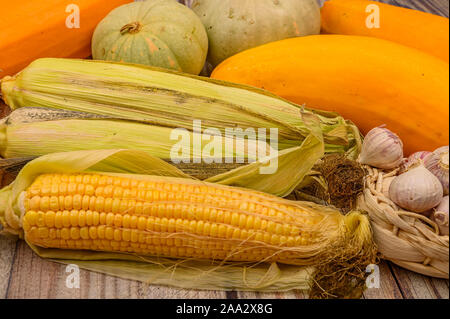 An unshelled ear of corn, young garlic in a wicker basket, marble pumpkins and yellow zucchini on the table. Autumn harvest. Healthy diet. Fitness die Stock Photo