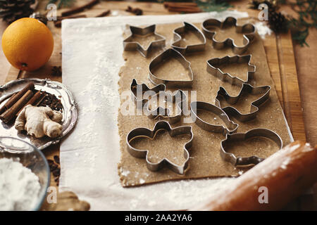 Making christmas gingerbread cookies. Raw dough with metal cutters for cookies and wooden rolling pin, anise, ginger, cinnamon, pine cones, fir branch Stock Photo