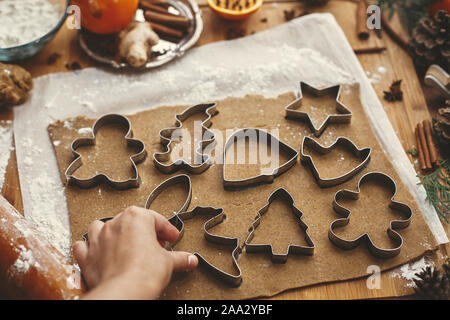 Hand cutting raw dough with  metal cutters and anise, ginger, cinnamon, pine cones, fir branches on rustic table. Making christmas gingerbread cookies Stock Photo