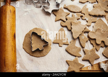 Making christmas gingerbread cookies, flat lay. Raw dough in shape of christmas tree and metal cutters, wooden rolling pin, anise, ginger, cinnamon, p Stock Photo