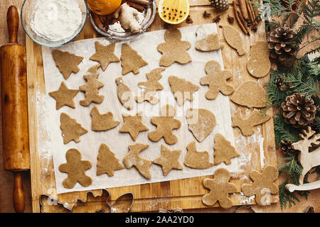 Making christmas gingerbread cookies, flat lay. Raw dough in different shapes cookies and wooden rolling pin, anise, ginger, cinnamon, pine cones, fir Stock Photo