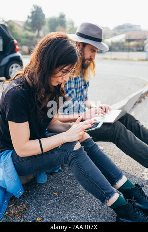 Young beautiful couple sitting outdoor using computer and smartphone - finance, banking, buying concept Stock Photo