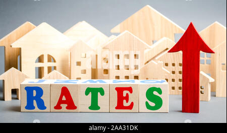 Wooden blocks with the word rates, up arrow and miniature houses. The concept of high interest rates on mortgages. Real estate. Credit. Loan Stock Photo