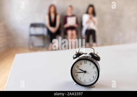 Closeup of mechanical clocks on table in office. Three women sits in chair on background. Selective focus. Stock Photo