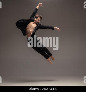 Man in casual office style clothes jumping and dancing isolated on grey background. Art, motion, action, flexibility, inspiration concept. Flexible caucasian ballet dancer, weightless jumps. Stock Photo