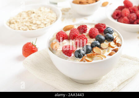 Tasty oatmeal porridge with raspberries, blueberries and nuts in bowl on white table, close up view Stock Photo