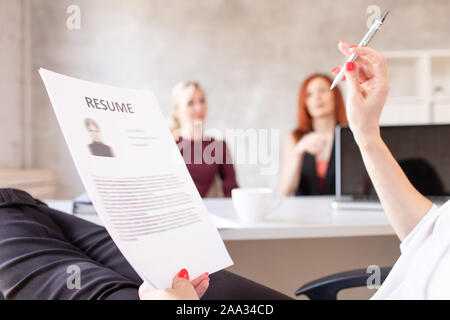 Closeup of resume in hands of HR with two women on background. Selective focus. Stock Photo