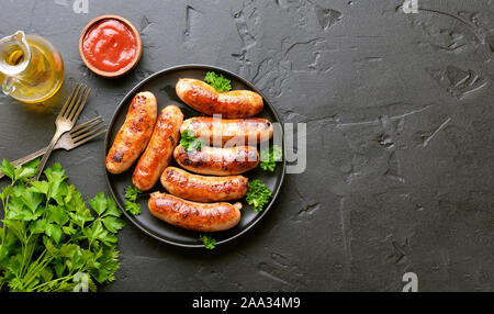 Barbecue sausage with fresh parsley on plate on a over black stone background with copy space. Top view, flat lay Stock Photo