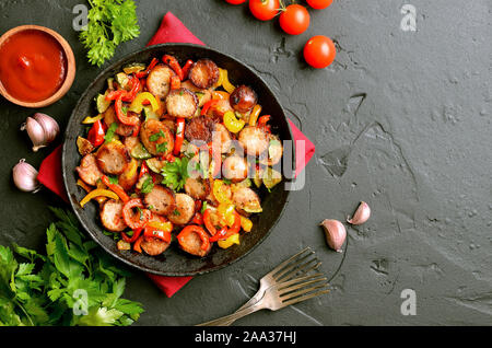 Slices of fried vegetables with sausages and spices in frying pan over black stone background with copy space. Top view, flat lay Stock Photo