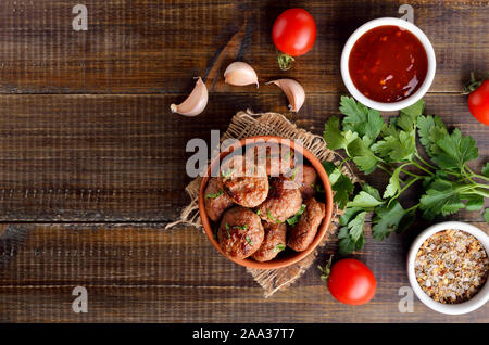 Homemade cutlets from minced meat in bowl and spices on wooden table. Top view, flat lay Stock Photo