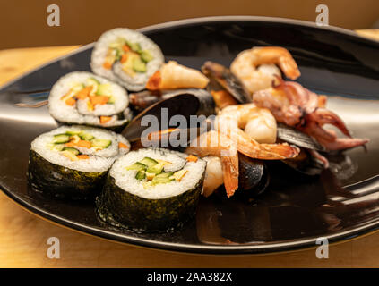 Sushi - rolls, shrimps and mussels on a black plate and wooden table Stock Photo