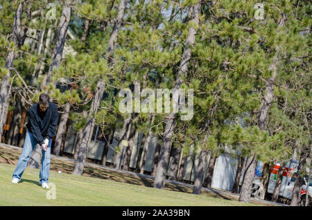 An intentionally tilted shot of a golfer chipping the ball towards the green from the fairway with an iron. Stock Photo