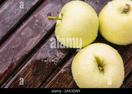 Golden apples covered by water drops on brown wet natural wooden table surface. Flat lay background with ripe fruits under rain with copy space. Autum Stock Photo