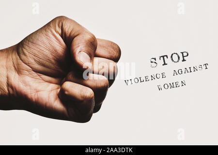 closeup of a man with his fist threateningly closed and the text stop violence against women against an off-white background Stock Photo