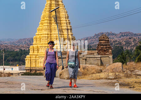 Girls travelers visiting the ruins of Hampi. The famous place of historical heritage of India. In the background is visible Virupaksha Temple Stock Photo