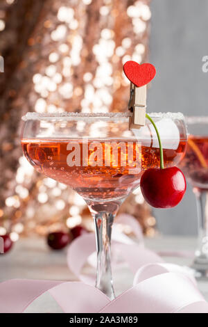 Two beautiful glasses with pink champagne and sweet cherry with heart shaped pin on it. Concept of shine party drinks Stock Photo