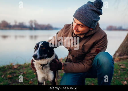 Man playing with dog in autumn park by lake. Happy pet having fun outdoors Stock Photo