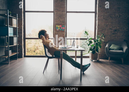 Profile side full body photo of peaceful joyful afro american girl freelancer finish her start-up project sit table dream stretch hands in loft office