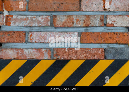 Brick wall close up. Rough garage texture. Background from bricks and yellow-black warning lines. Brick background close-up. Loft style. Stock Photo