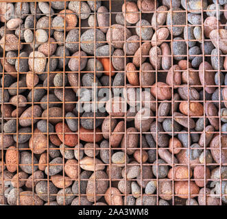 Pebble texture behind lattice. Round pebbles and metal mesh close-up. Unusual background from a grid with stones. Grunge texture. Stock Photo