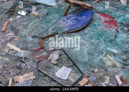 Broken glass. Fragments of construction dump. Ruined interior. Broken table, pieces of destroyed furniture, large pile of broken glass. Stock Photo