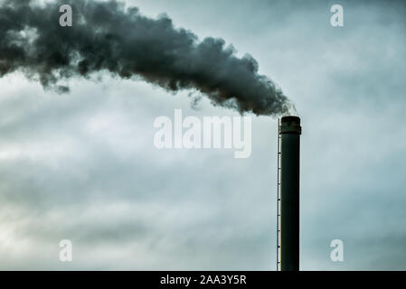 Black smoke on a grey sky with space copy , comming from a tall chimney. Denmark, November 10, 2019 Stock Photo