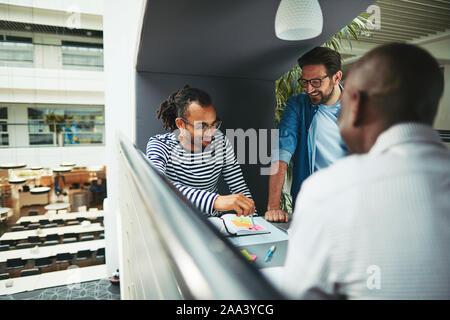 Diverse group of smiling businessmen going over notes together while working in an office meeting pod Stock Photo