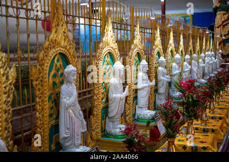 A long row of white Buddha images and offerings line the base of the massive reclining Buddha at the Chauk-htat-gyi Temple in Yangon, Myanmar (Burma) Stock Photo