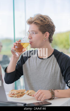 Man drinking beer. Side view of handsome young man drinking beer while eating a sandwich. Lifestyle concept. Stock Photo