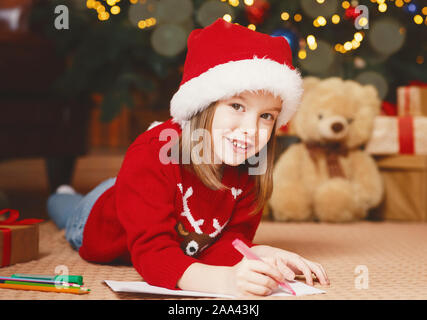 Smiling little girl in xmas hat writing letter to Santa Stock Photo