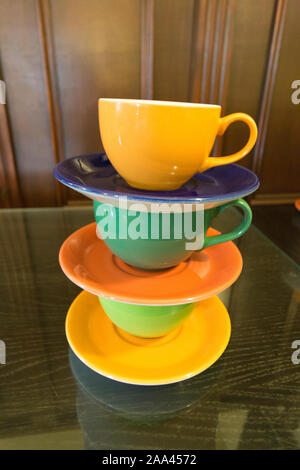 Brightly coloured cups and saucers, stacked in piles ready for use. Stock Photo