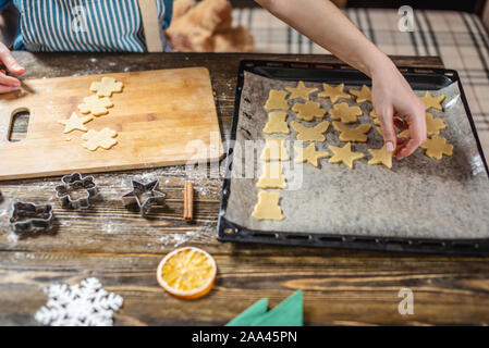 A woman rolls out the dough with a rolling pin and shapes it with her hands for a festive gingerbread on a wooden table background. Christmas mood for Stock Photo