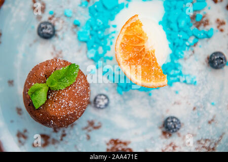 Chocolate fondant dessert pudding with blue ice cream on plate with orange. Stock Photo