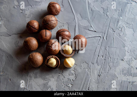 Pile macadamia nuts open kernels and shells on gray concrete background, top view. Stock Photo