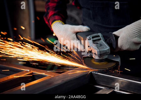 Worker hand with electric wheel grinding on steel structure in factory, light spark. Stock Photo